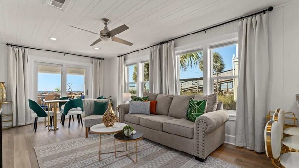 A spacious living area with a sofa, coffee table, and dining set. Large windows offer a view of the outdoors.