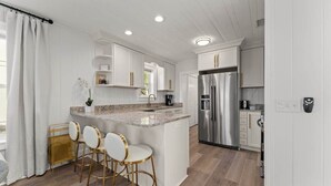 A modern kitchen with white cabinetry, a stainless steel refrigerator, and a granite countertop island with bar stools.