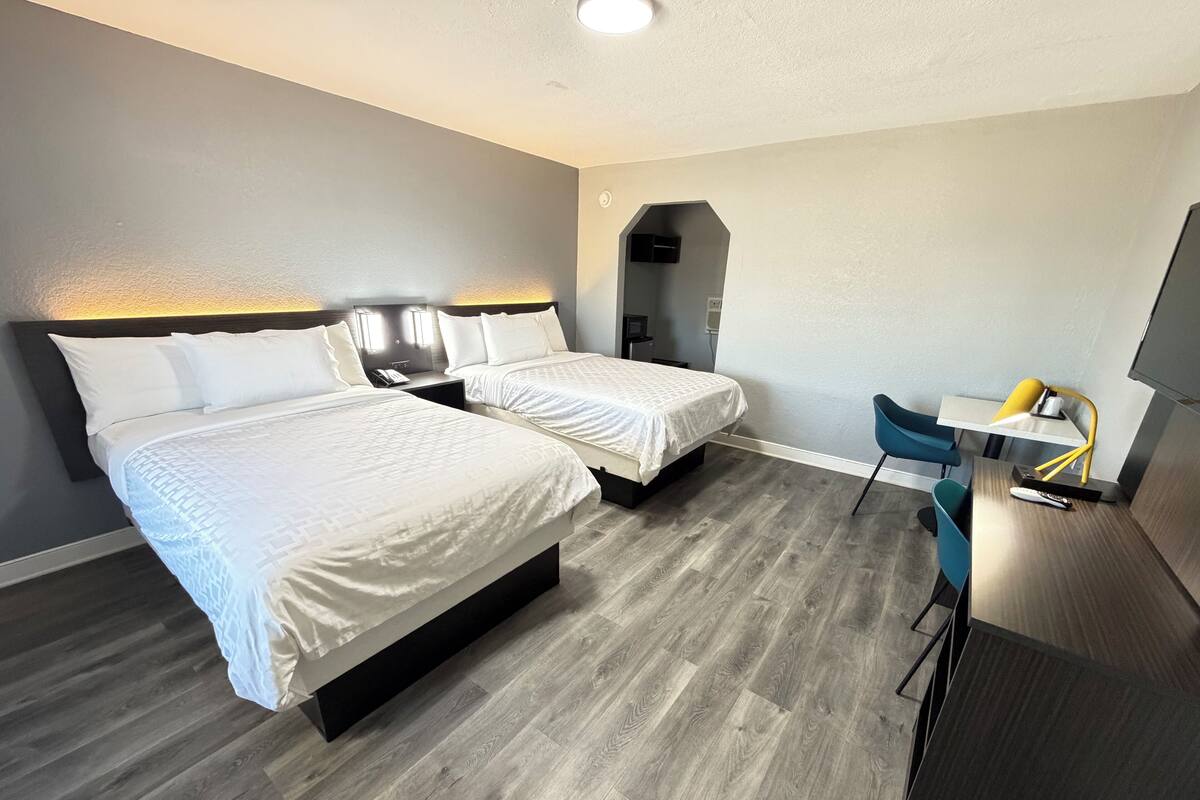Une chambre d’hôtel avec deux lits, un bureau avec une chaise et un téléviseur.