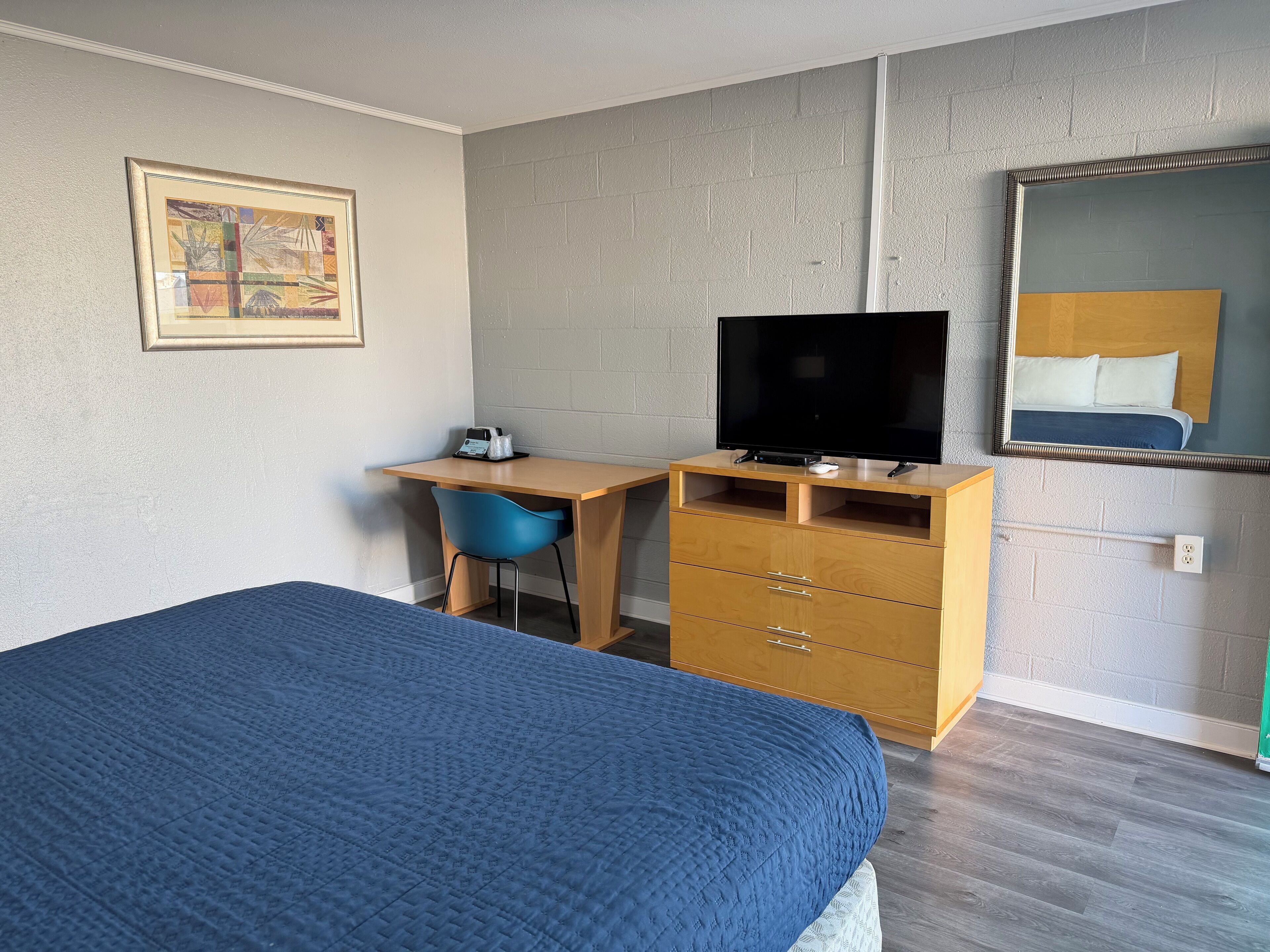 A hotel room with a bed, a desk with a chair, a television, and a dresser.