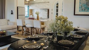 Un comedor moderno con una mesa negra dispuesta para cuatro, una cocina al fondo y una sala de estar con sofá y sillones.