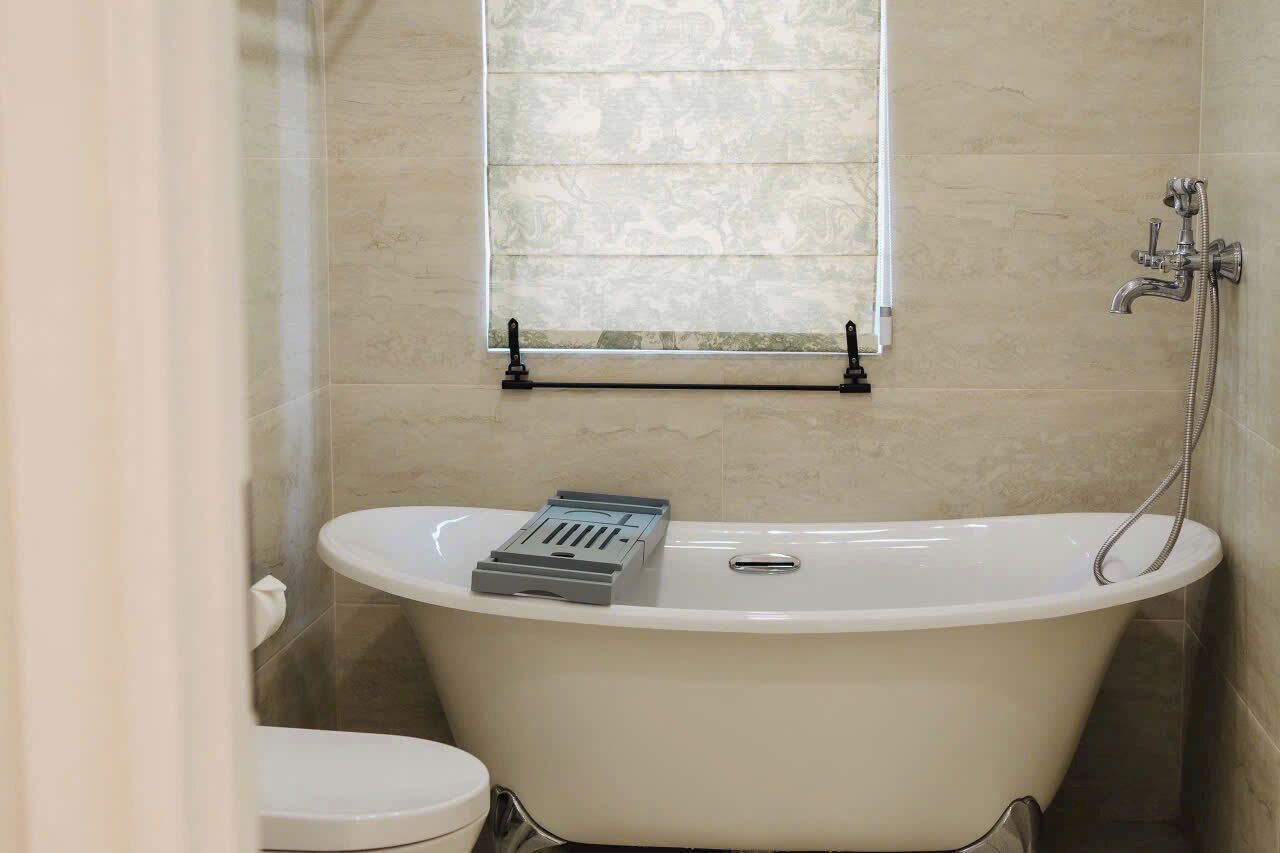 A bathroom with a freestanding bathtub, a toilet, and a window with blinds.