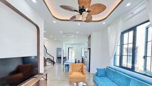 Un salón espacioso con un televisor de pantalla plana grande, un sofá azul, una mesa de centro de madera y un ventilador de techo.