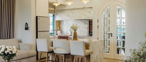 A modern kitchen with a marble countertop, a central island with bar stools, and pendant lighting.