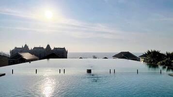 An infinity pool with a clear view of a large building and the ocean in the background.