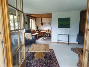 Un salon chaleureux avec une table basse en bois, un fauteuil bleu et un coin repas comprenant une table et des chaises en bois.