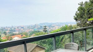 Un balcon avec une table et des chaises, donnant sur un paysage urbain avec des bâtiments et de la verdure.
