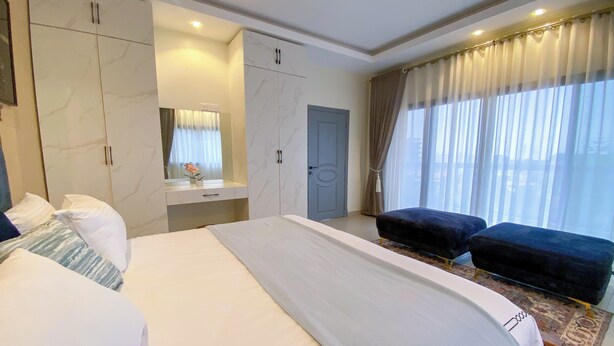 Une chambre d’hôtel moderne dotée d’un grand lit, d’un coin salon, d’une armoire, d’une coiffeuse avec un miroir et d’une grande fenêtre avec des rideaux.