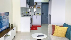 Un espace de vie compact comprenant un coin cuisine, un canapé avec des coussins, une table basse et un téléviseur posé sur un meuble.