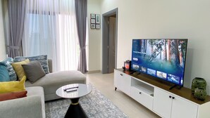 Un salon avec un canapé, une table basse, un téléviseur posé sur un meuble et un tapis à motifs.