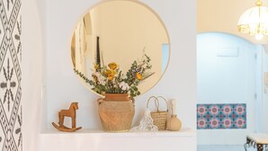 En hvid væg med et rundt spejl, en vase med blomster, en trækhest i træ, en flettet kurv og en lille flaske.