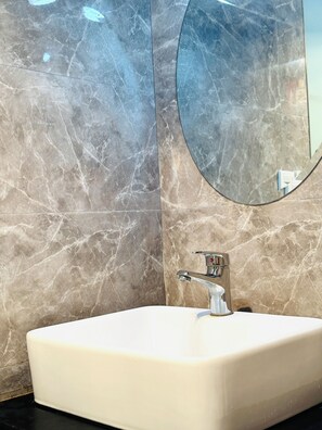 A bathroom with a white sink, a round mirror, and marble walls. - Chongqing Justom Family Serviced Apartments 1 (Chongqing)