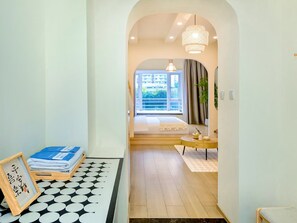 Un pasillo que conduce a un dormitorio con un gran ventanal, piso de madera y una mesa redonda con una planta.