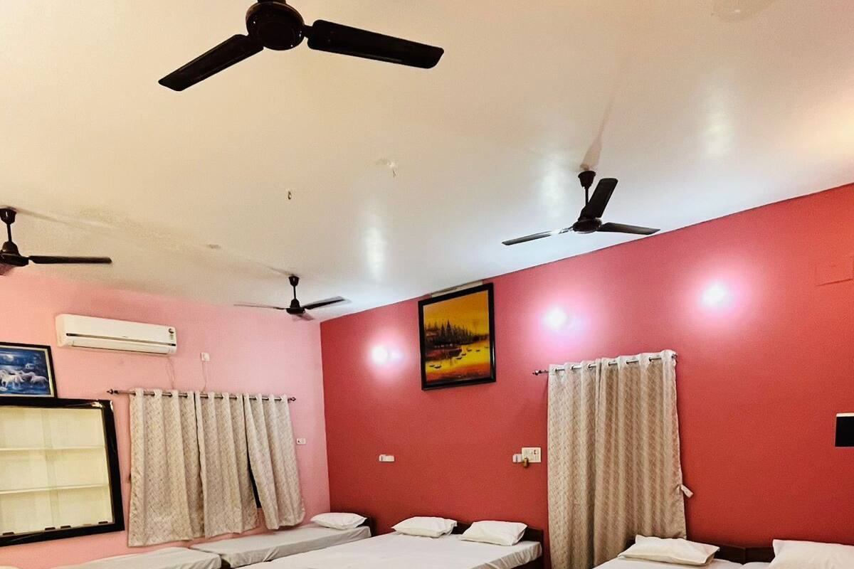 A hotel room with four single beds, a ceiling fan, an air conditioning unit, and a painting on the wall.