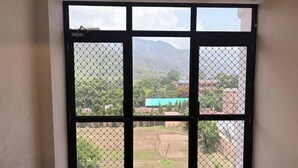 A room with a large window featuring a black metal grid. - Hotel Hitam (Rishikesh)