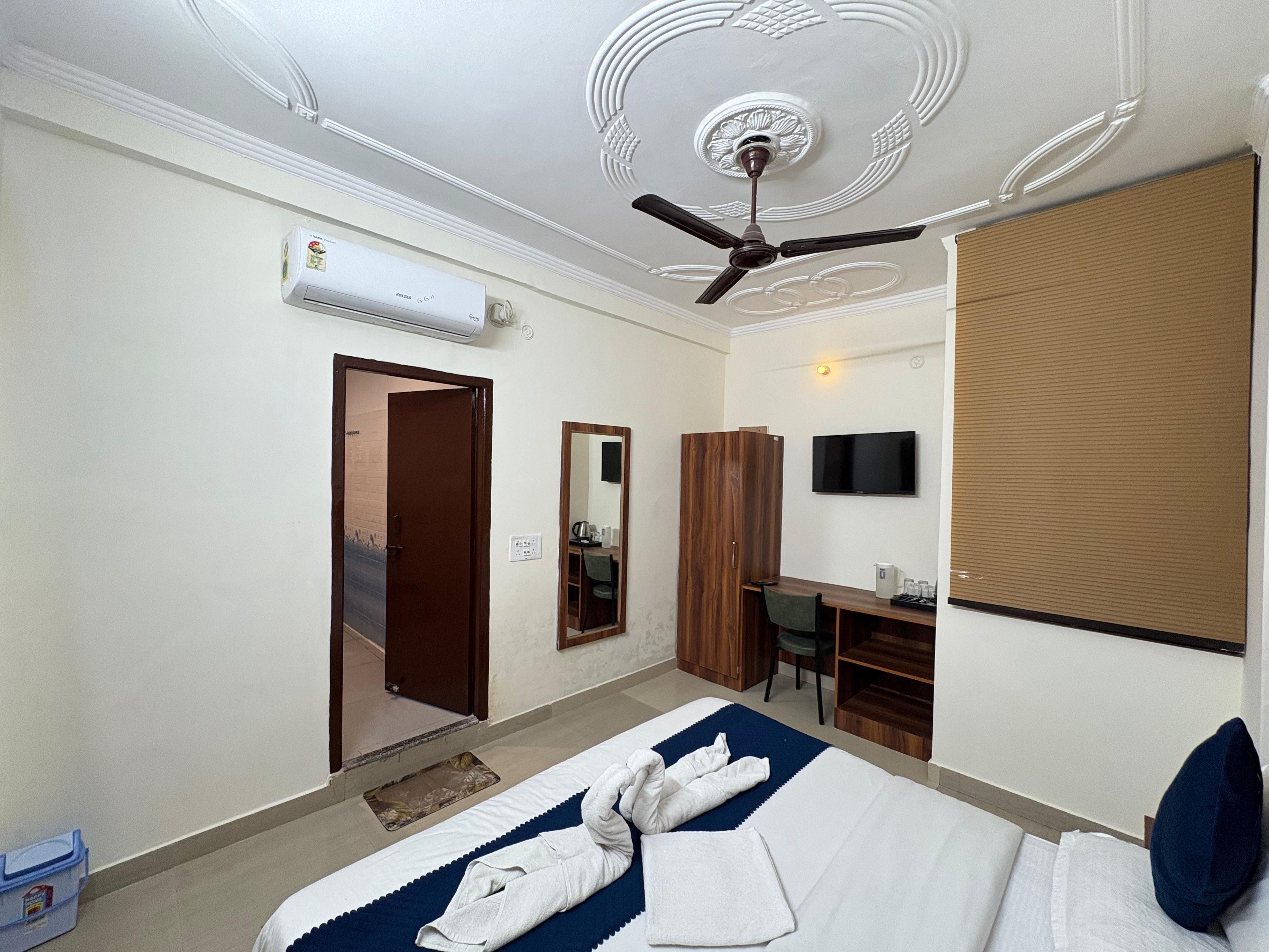 A hotel room with a bed, a desk, a chair, a television, and an air conditioning unit.