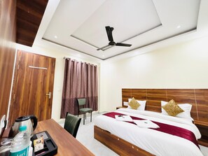 A hotel room with a bed, a desk, a chair, a coffee maker, and a ceiling fan. - Hotel Hitam (Rishikesh)