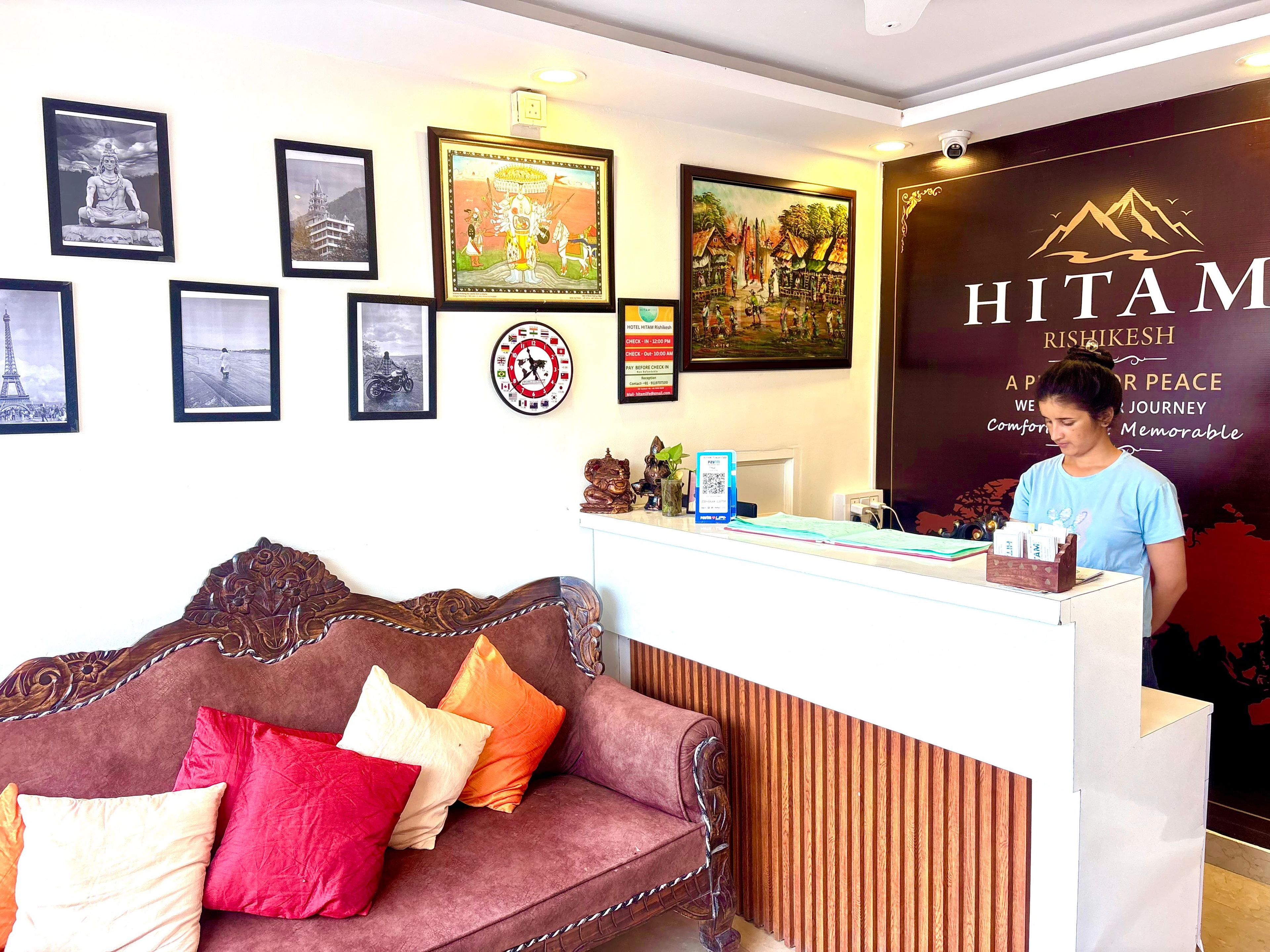 A reception desk with framed pictures, a clock, and a sign for Hitam Rishikesh.