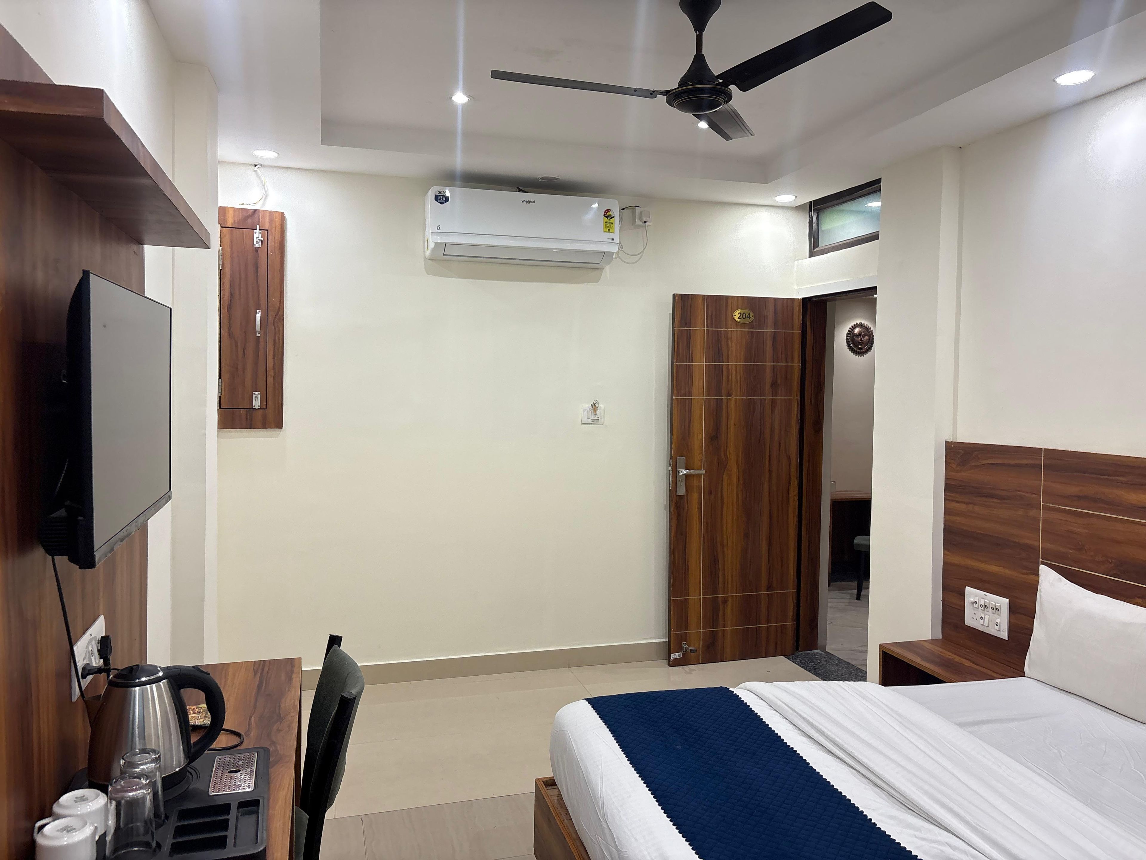 Une chambre d’hôtel équipée d’un lit, d’une télévision, d’un climatiseur, d’un ventilateur de plafond et d’une armoire en bois.