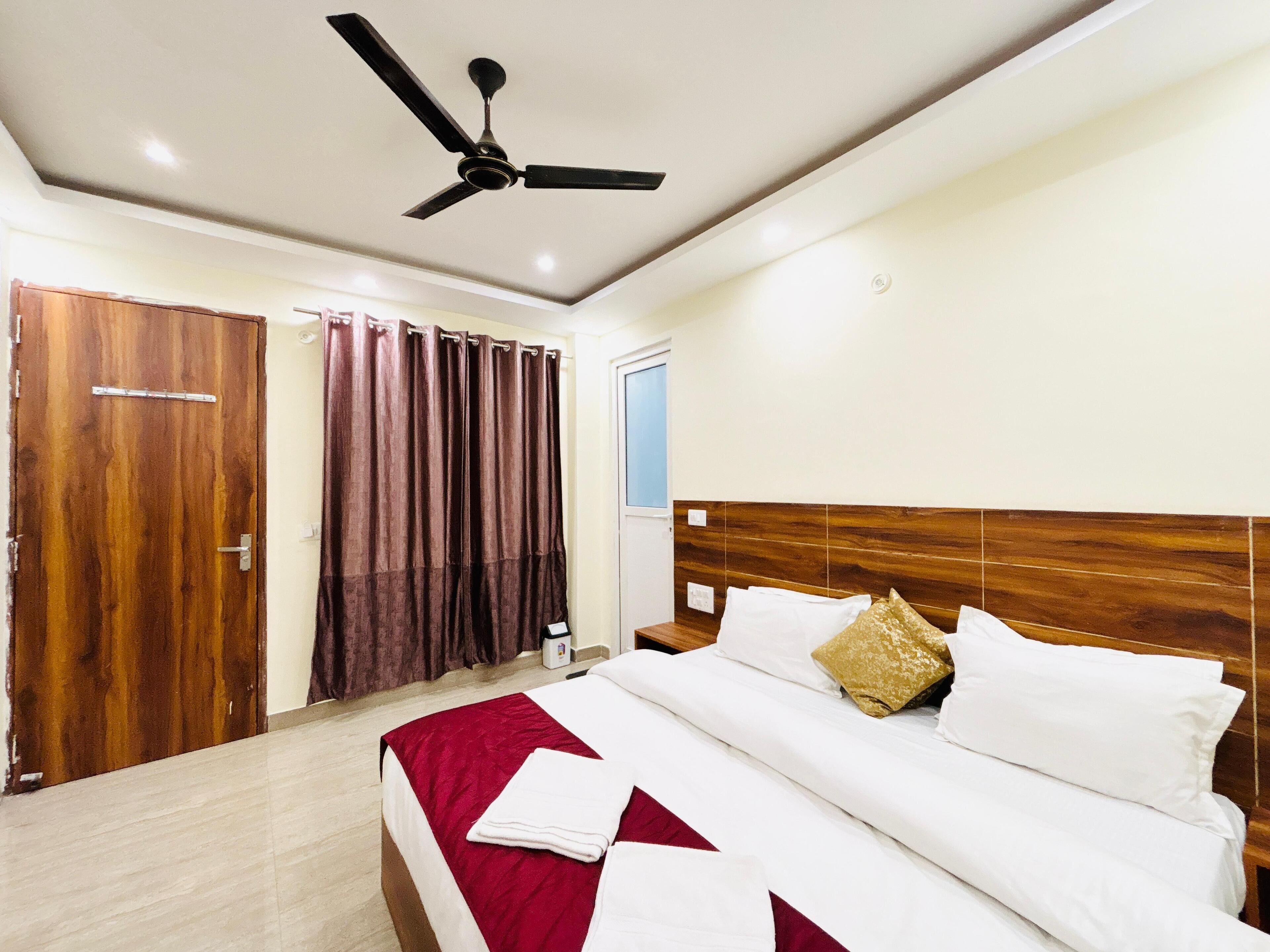 A hotel room with a bed, a ceiling fan, a wooden door, and a window with curtains.
