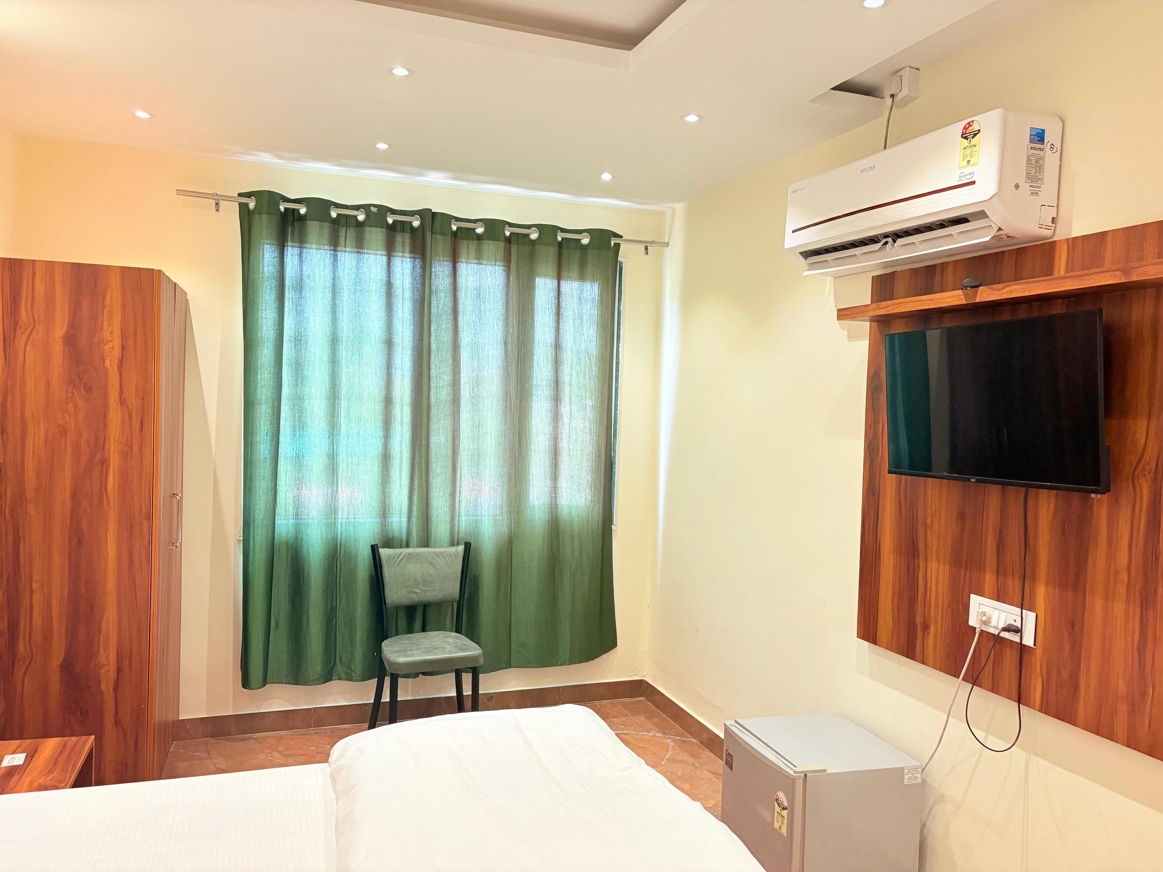 A hotel room with a bed, a chair, an air conditioner, a television, and a small refrigerator.
