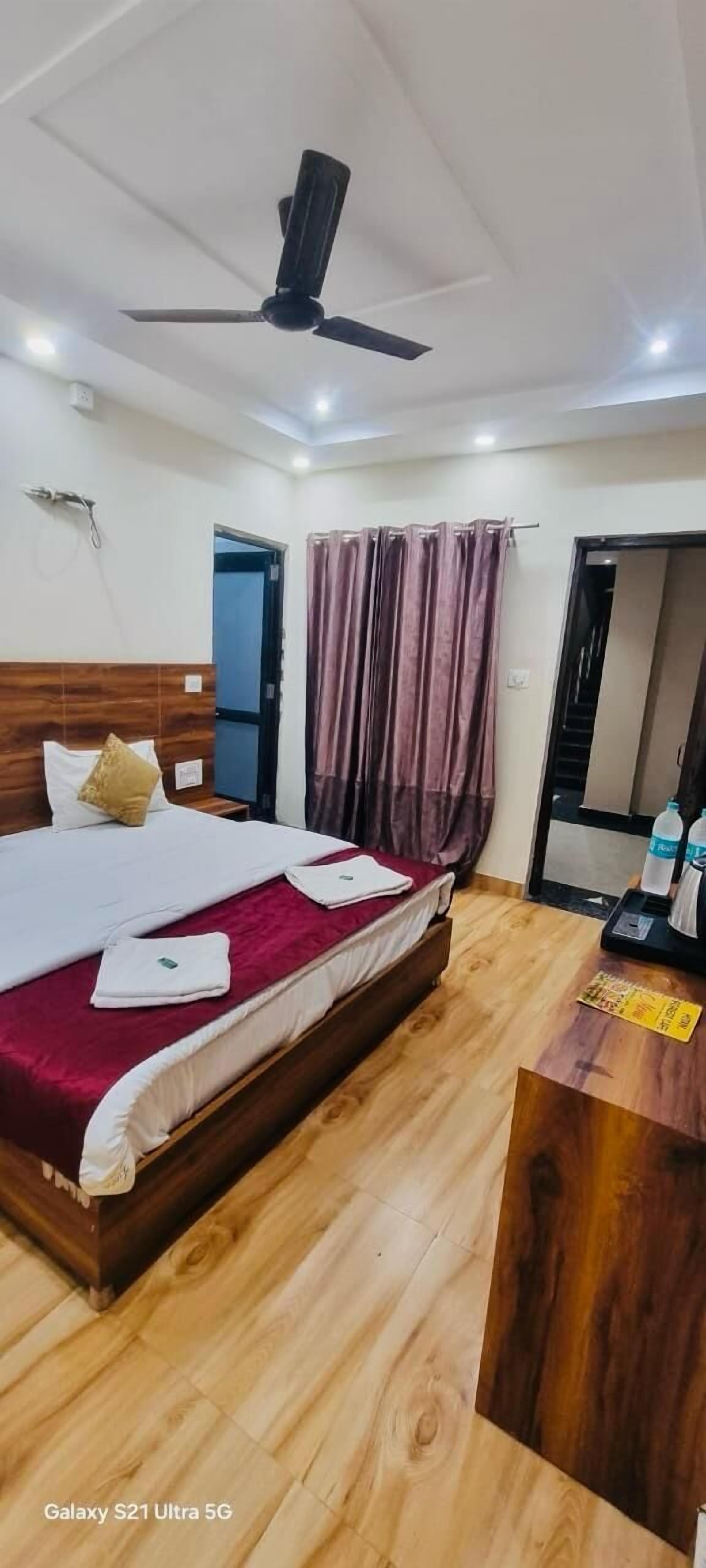 Une chambre d’hôtel avec un lit en bois, un ventilateur de plafond, un bureau avec un miroir et une fenêtre avec des rideaux.