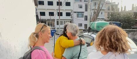 Un grupo de personas de pie en una acera, con edificios y líneas eléctricas al fondo.