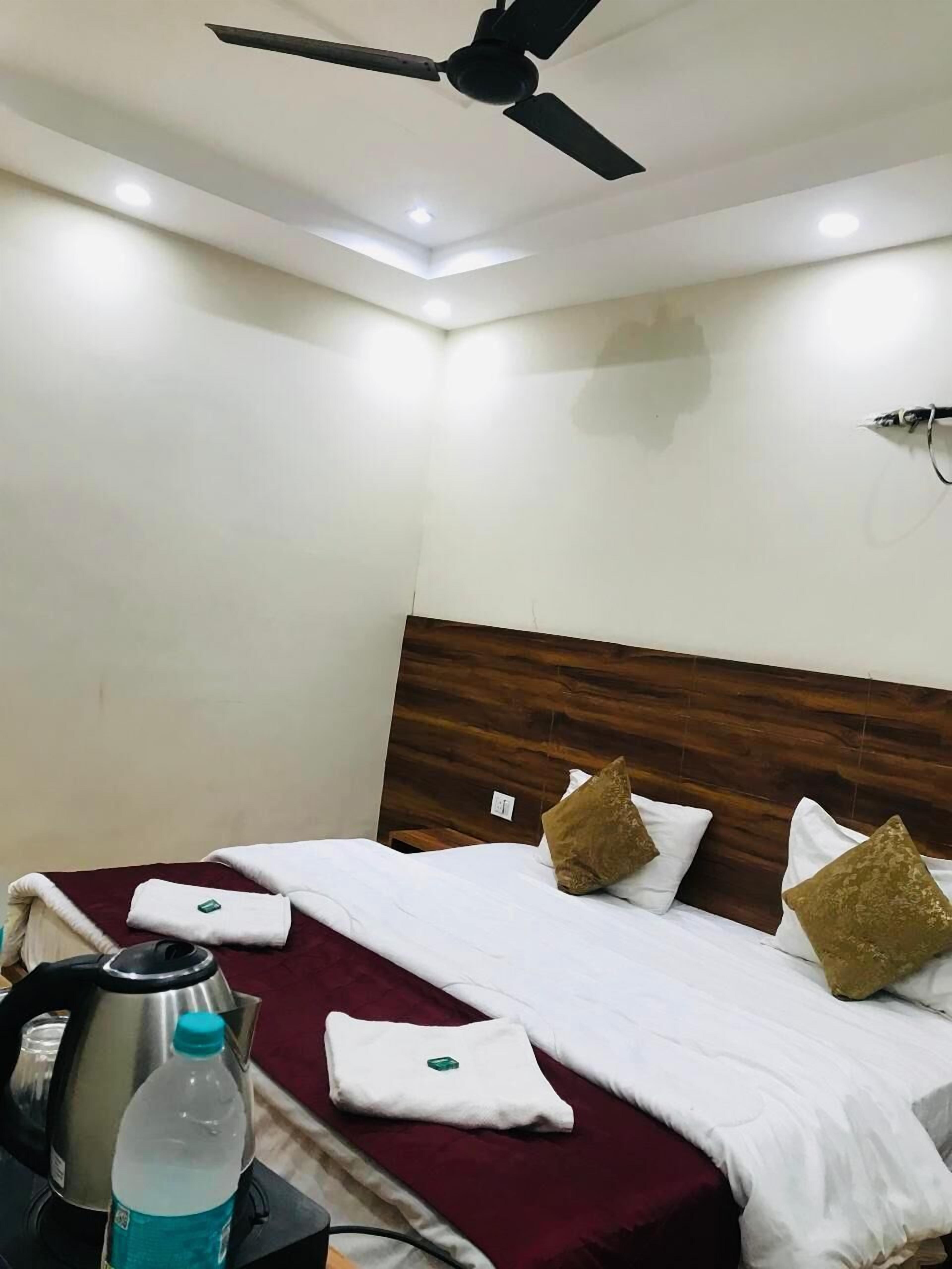 Quarto de hotel com cama, almofadas, chaleira, garrafa e ventilador de teto.