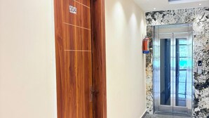 A hallway with a wooden door labeled "304", a marble wall, and an elevator. - Hotel Hitam (Rishikesh)