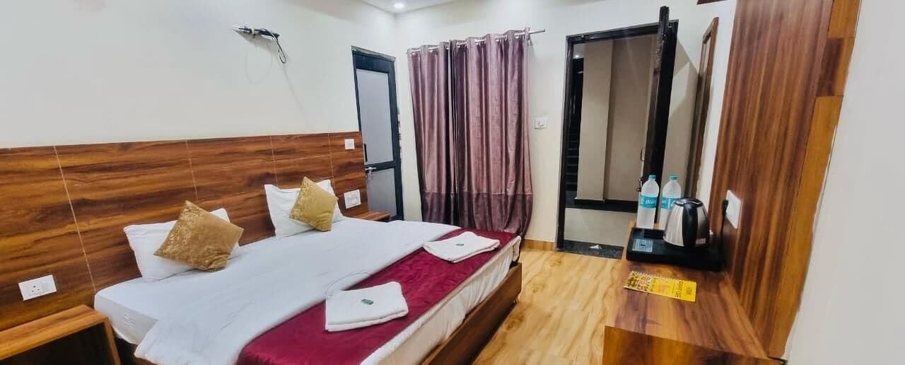 A hotel room with a wooden headboard, two beds with white linens, a red throw blanket, a wooden side table, a mirror, and a door with a curtain.