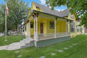 A yellow house with a porch, a front door, and a small front yard with a flagpole. - Maple Manor City Scene (Spokane)