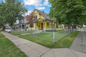 A yellow house with a porch, surrounded by a chain-link fence, and a sidewalk in front. - Maple Manor City Scene (Spokane)