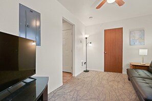 A living room with a flat-screen TV, a sofa, a floor lamp, and a wooden door. - Maple Manor City Scene (Spokane)