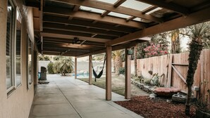 A covered patio with a concrete floor, wooden beams, and a view of a backyard with a wooden fence, plants, and a hammock. - Spacious 4BDRM with a Stunning Pool+Game Room and Firepit (Bakersfield)