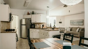 A modern kitchen with white cabinets, a stainless steel refrigerator, and a dining area with a wooden table and chairs. - Spacious 4BDRM with a Stunning Pool+Game Room and Firepit (Bakersfield)