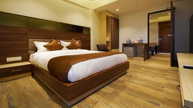 A modern hotel room with a large bed, wooden headboard, and a desk with a chair. - Hotel 4 Point (Gandhinagar)
