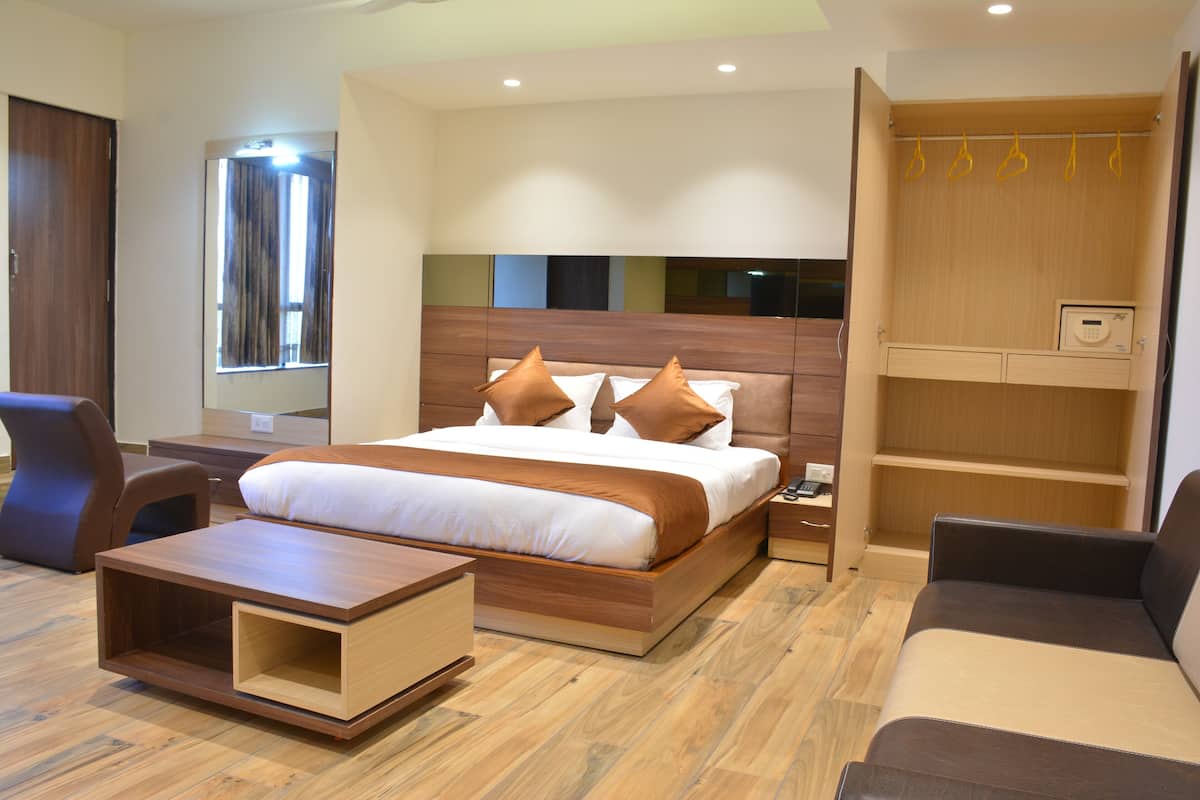 Una habitación de hotel moderna con una cama grande, una mesita de noche de madera, un banco de madera, un armario y una ventana con cortinas.