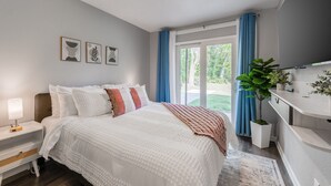 Ein Schlafzimmer mit einem großen Bett, einem Nachttisch, einer Kommode und einem Fenster mit Vorhängen.