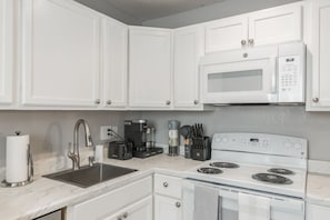 Una cucina con mobili bianchi, un lavello in acciaio inossidabile, un forno a microonde, una macchina da caffè e un fornello.