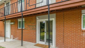 Ein Backsteinhaus mit Balkon, einer Tür mit Glasscheibe und einer Fußmatte mit der Aufschrift 'COME IN'.