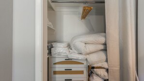 Ein ordentlich organisierter Kleiderschrank mit weißen Schubladen und Regalen, der gefaltete Decken und eine Kleiderstange mit hölzernen Kleiderbügeln enthält.