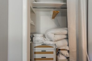 Un armadio ordinato con cassetti e ripiani contenitori bianchi, con coperte piegate e un attaccapanni con grucce in legno.
