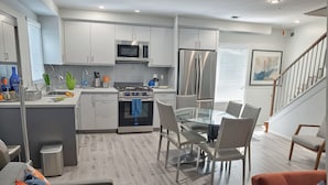A modern kitchen with stainless steel appliances, a dining area with a glass table and chairs, and a staircase leading to an upper level. - Prime Hollywood 4BR Suite Stay Near Paramount: Free Parking (Los Angeles)