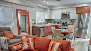 A modern living room with a sofa, a dining table, and a kitchen in the background. - Prime Hollywood 4BR Suite Stay Near Paramount: Free Parking (Los Angeles)