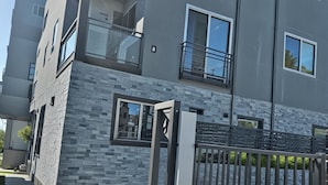 A modern multi-story residential building with a stone facade, balconies, and a gated entrance. - Prime Hollywood 4BR Suite Stay Near Paramount: Free Parking (Los Angeles)