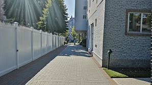 A paved pathway leading to a modern building with a brick facade and a white fence on one side. - Prime Hollywood 4BR Suite Stay Near Paramount: Free Parking (Los Angeles)