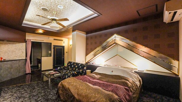Habitación de hotel con cama, escritorio, silla, ventilador de techo y una ventana grande.