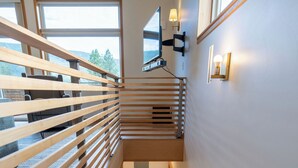 Eine hölzerne Treppe mit Geländer, die zu einer zweiten Etage mit großen Fenstern und Wandleuchten führt.