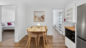 A modern kitchen with a wooden dining table, chairs, and a refrigerator. - Garigal Retreat with Pool access (Forestville)