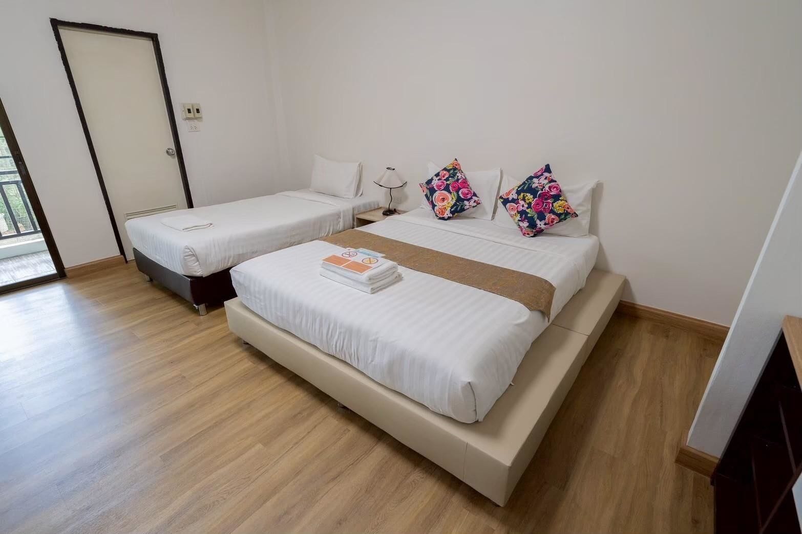 A hotel room with two single beds, a large bed, and a wooden floor.